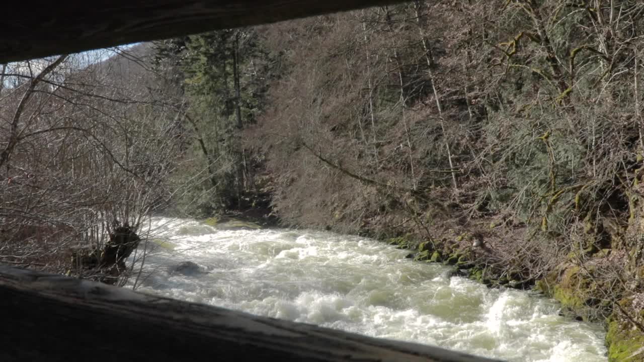 shot from top to bottom blocked by wooden bridge. Water flowing from the dam channel. view of the river channel. video of water waves from an overflowing river in Creux Du Van, Neuchatel, Switzerland.
