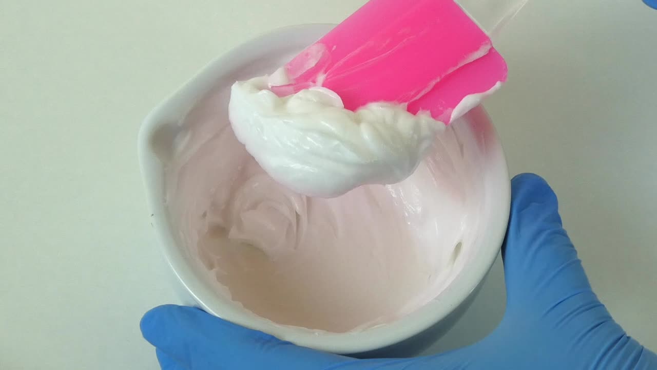 Macro shot of a cosmetic laboratory process where gloved hands in blue gloves mix a cream using a porcelain mortar and pestle.
