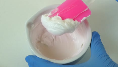 macro shot of a cosmetic laboratory process where gloved hands in blue gloves mix a cream using a porcelain mortar and pestle.