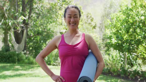 Portrait-of-asian-woman-holding-a-yoga-mat-smiling-while-standing-at-the-park