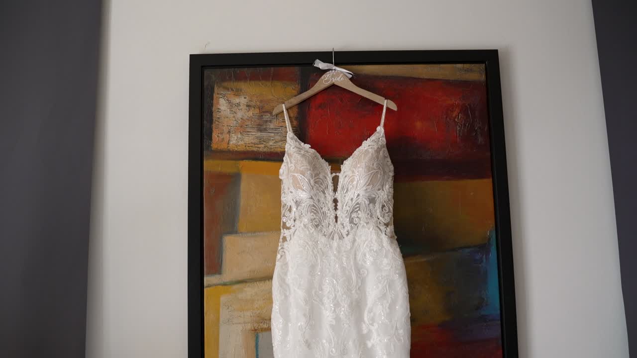 A stunning bridal dress is displayed on a hanger against an abstract art background in a contemporary setting. The intricate lace design shines in soft light, creating a perfect view