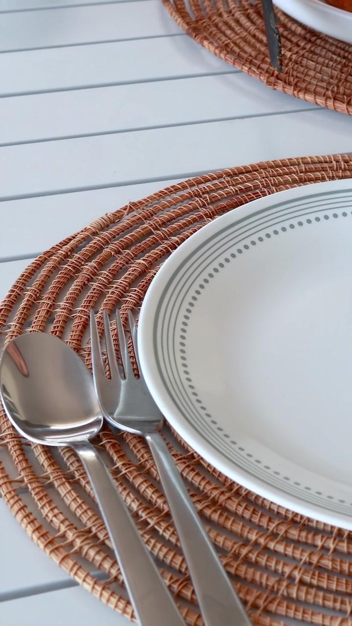 A table is set with fried chicken, a plate, and cutlery on a woven mat. Bright, natural lighting enhances the scene