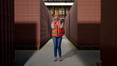 full body of asian female engineer with safety helmet smiling to camera and saying wow while standing with red brick packed in stacks are stored