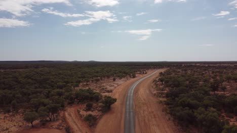 Drohne-Steigt-über-Eine-Sehr-Abgelegene-Landstraße-Auf,-Umgeben-Von-Roter-Erde-Und-Bäumen-Im-Australischen-Outback