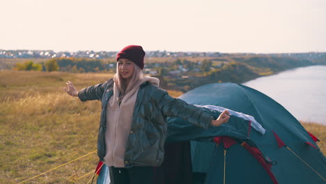 girl-hiker-goes-out-of-tent-stretching-against-sky-and-river