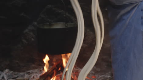 georgian woman rinsing cheese curd strings in whey by old fireplace