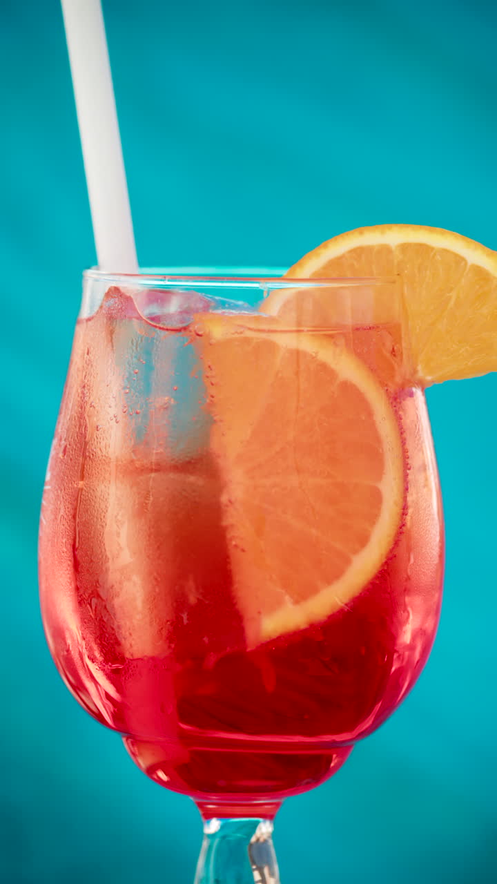 Close up of an orange slice and ice cubes in a glass of red orange with condensation. Vertical