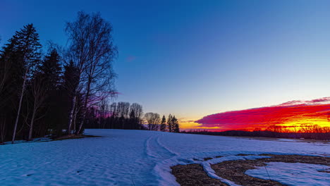 Vista-Estática-De-La-Llegada-De-La-Temporada-De-Primavera-Con-Nieve-Derritiéndose-Sobre-Tierras-De-Cultivo-Rodeadas-De-árboles-Durante-La-Puesta-De-Sol-En-Timelapse