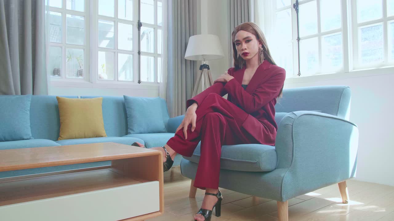 Young Fashion Transgender Woman Wearing Red Clothes Sitting On Sofa And Posing In Home