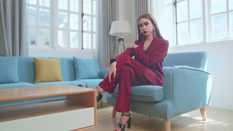 young fashion transgender woman wearing red clothes sitting on sofa and posing in home
