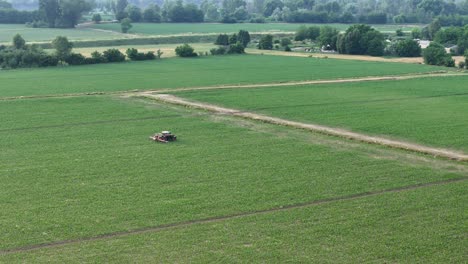 real-time drone orbit around a tractor with boom sprayer operating in a green maize field close to rural houses, capturing the precise movement of crop treatment and the vibrant countryside landscape