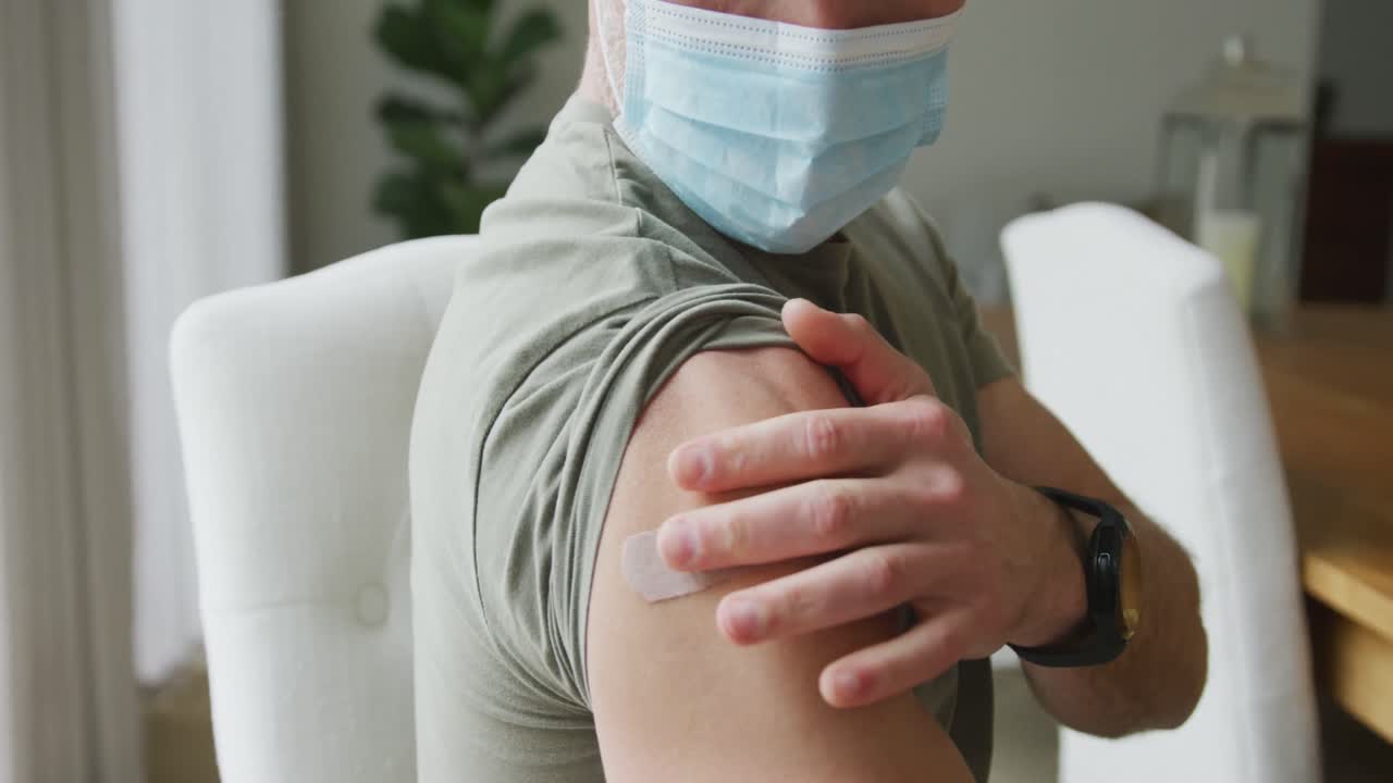 Caucasian man wearing face mask and checking his bandage in living room