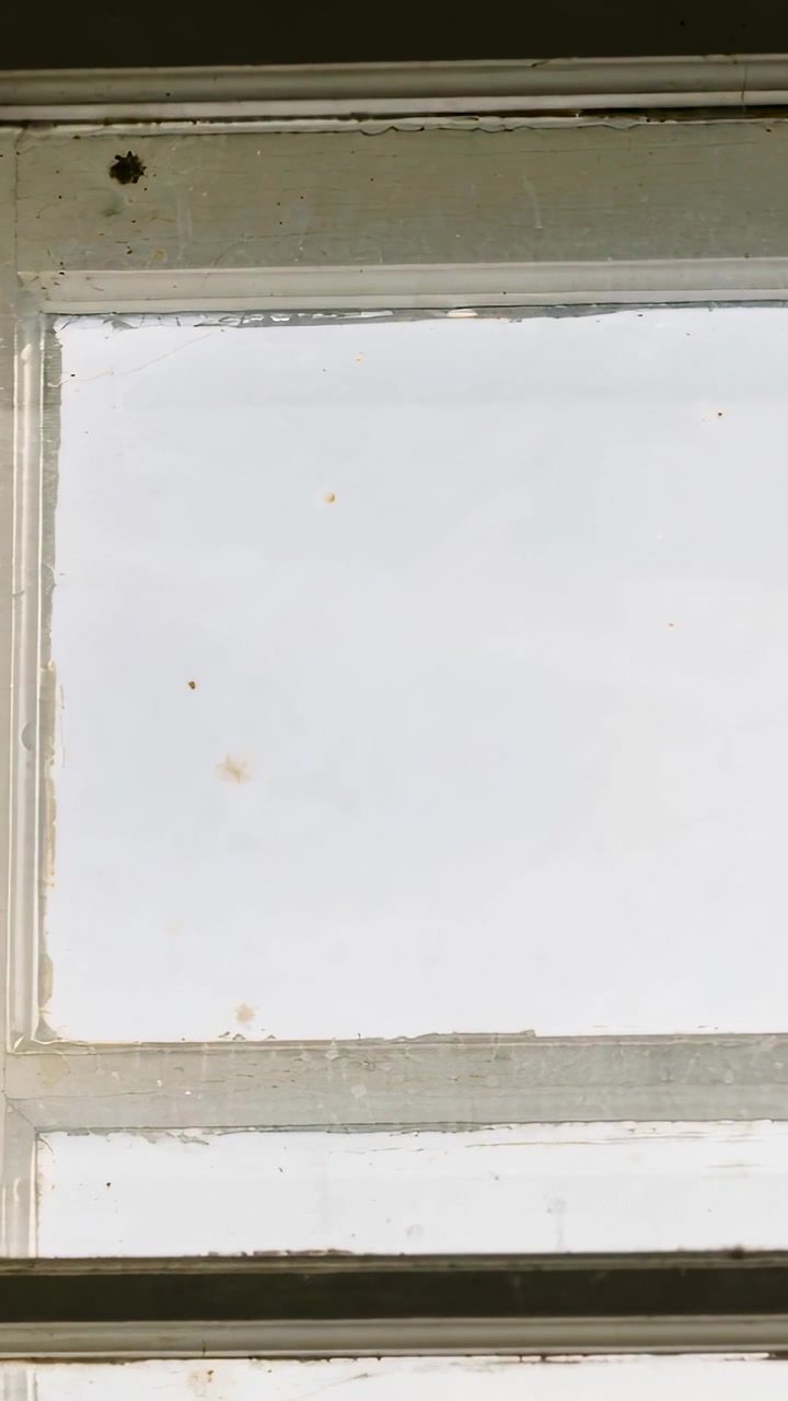 Vertical video: Panning camera past wooden window inside, revealing sash, spiderweb and paint wear
