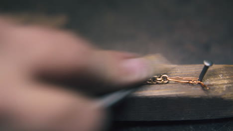 jeweler polishes gold chain on wooden gutter at table close