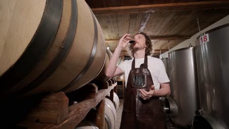 authentic shot of successful male sommelier is tasting a flavor and checking white wine quality poured in transparent glass in a wine cellar.