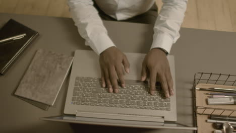 vista superior de las manos de un hombre de negocios estadounidense irreconocible escribiendo en el teclado de una computadora portátil en el lugar de trabajo