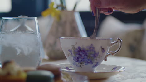 Revolviendo-Una-Taza-De-Té-De-Flores-Moradas-Vintage