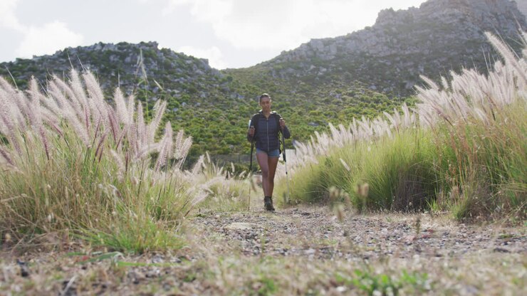 African american woman with trekking poles walking while trekking in the mountains