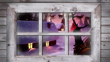 marco de ventana de madera contra la nieve que cae sobre varias casas y árboles en el paisaje de invierno