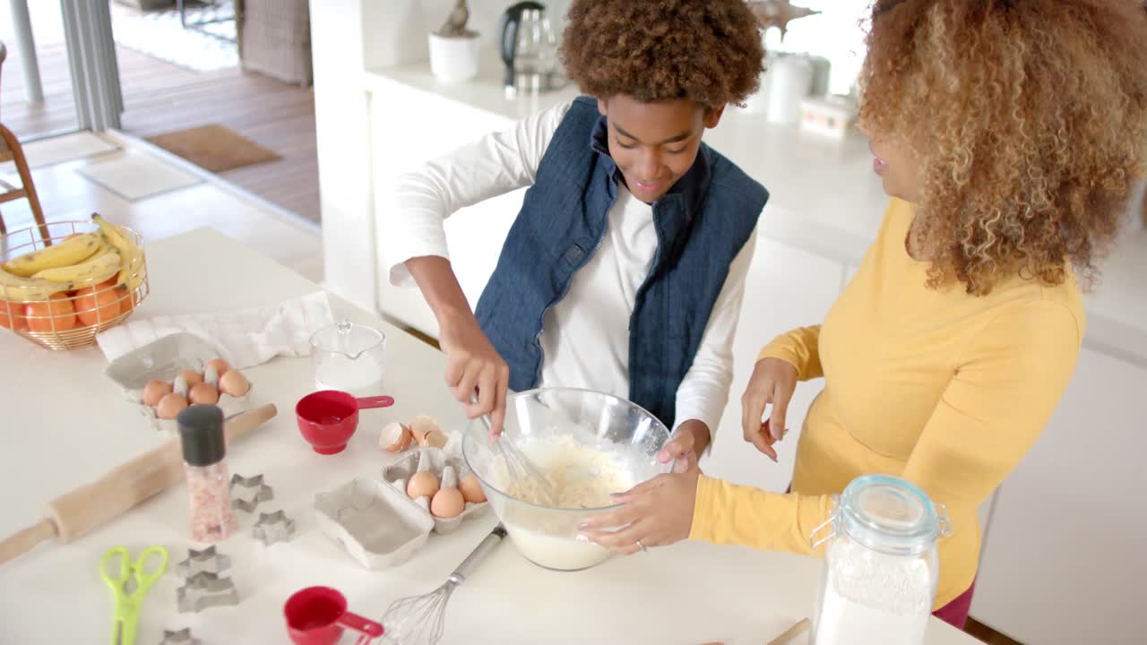 Happy african american mother and son baking in kitchen, slow motion