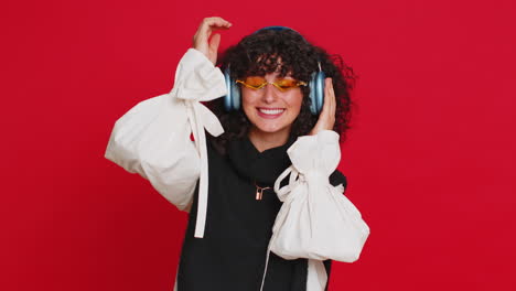 woman listening music on headphones, dancing disco fooling around having fun on red background