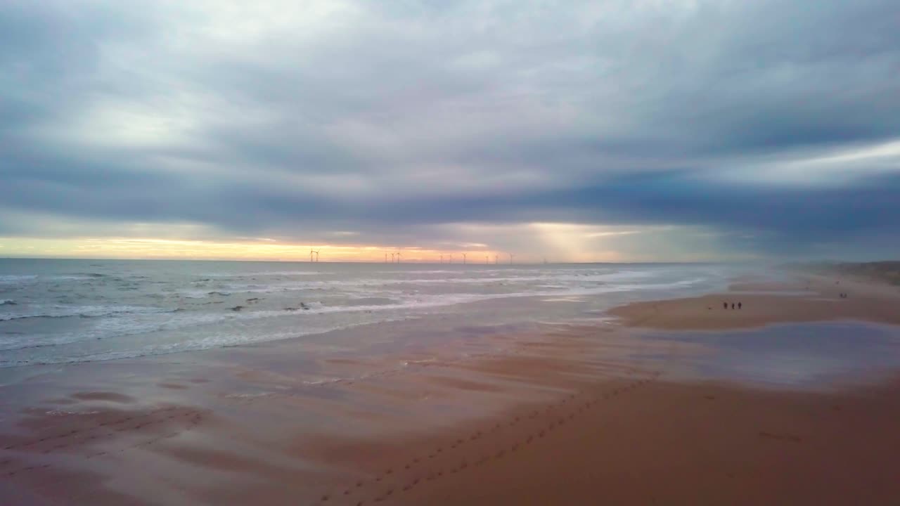 A quiet beach scene at sunset in Scotland with gentle waves and distant wind turbines