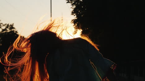 chica con el pelo largo divirtiéndose al atardecer agitando la cabeza jugando con el pelo bajo los rayos del sol