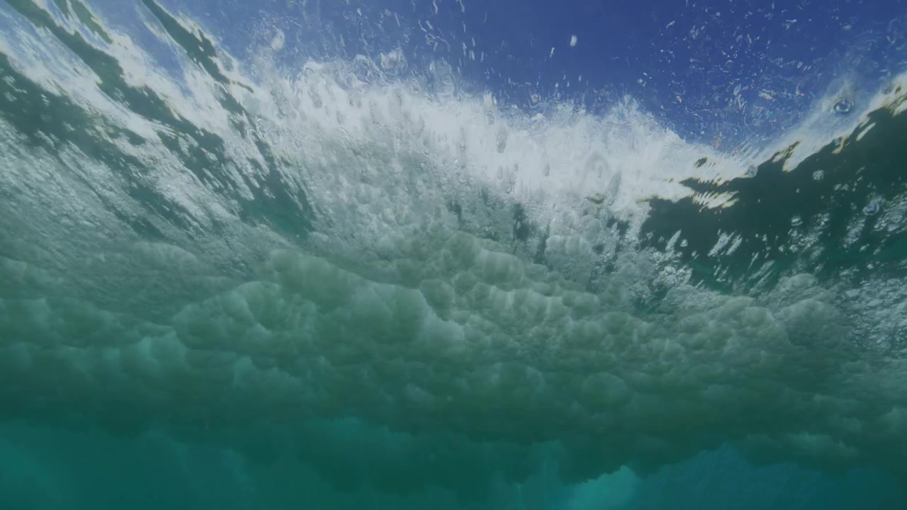 Backside of a breaking wave sweeps overhead through clear turquoise ocean water from below