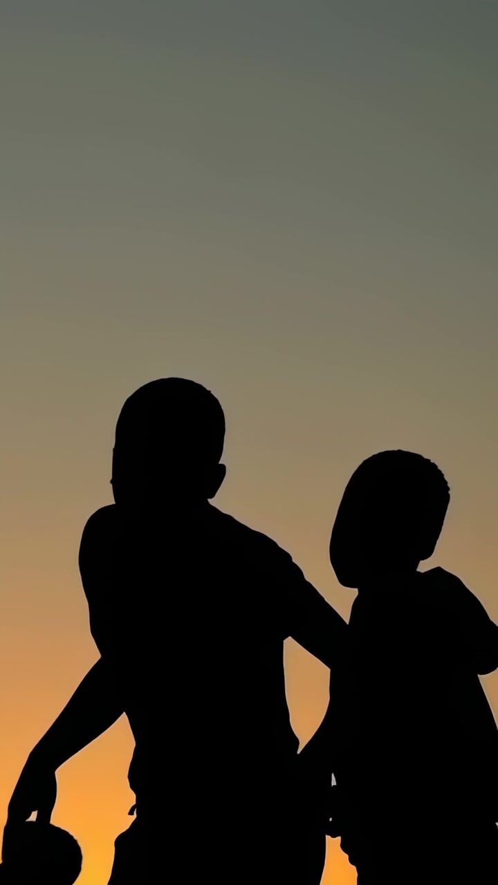 3 ragazzi si muovono nel cielo al crepuscolo; il terzo entra da destra, unendosi a un vivace gruppo che gioca vicino a delle lampade per l'istruzione.