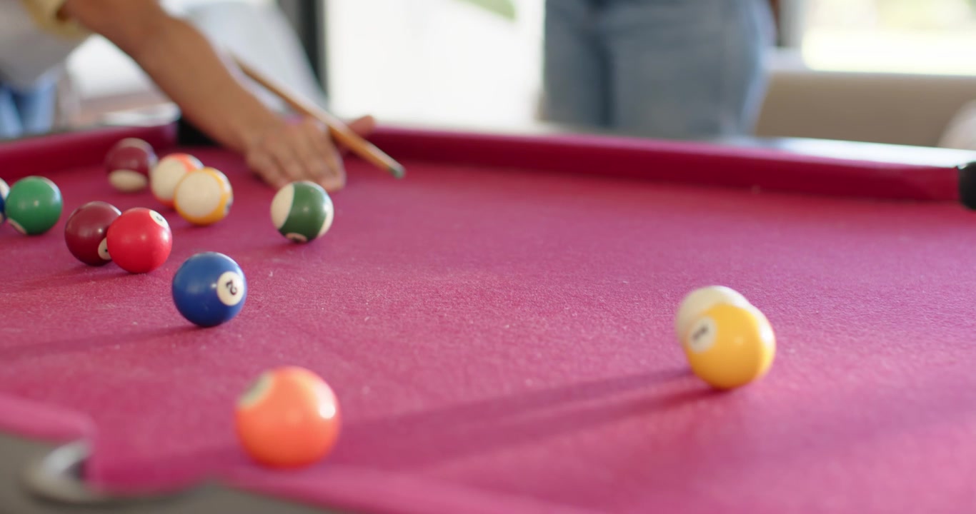 African American couple watching woman lining up, striking cue ball on red-felt table for leisure