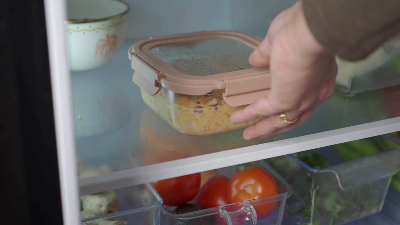Hand Placing Food Container into a Refrigerator