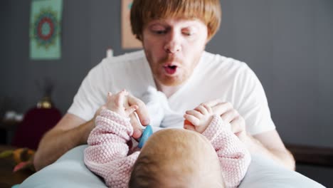 playful dad grimacing and soothing baby daughter with toy