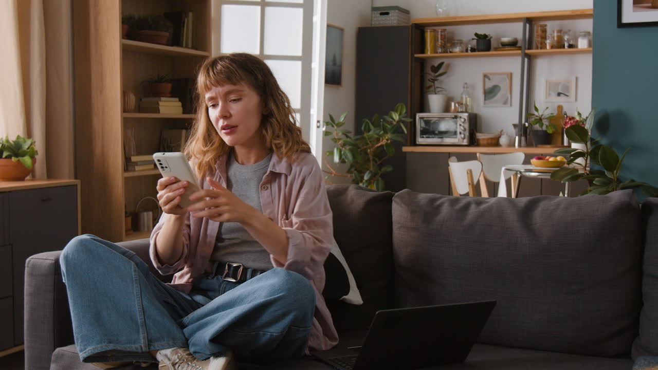 Woman using mobile phone and laptop on couch