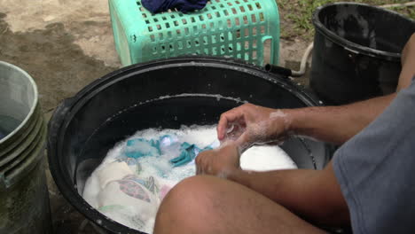 man's hand washing dirty clothes with bubbles in black basin