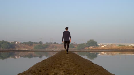 man walking in a peaceful lake with reflections of local trains travelling in indian railway in mumbai - wide shot