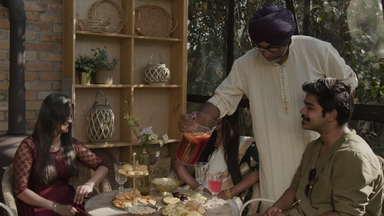 An Indian family and friends gathering, enjoying drinks and snacks on a patio