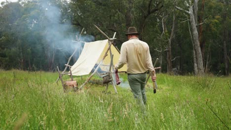 australian bushman walks with a skinned rabbit to his historical looking hut in the bush