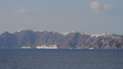 a view of the majestic black cliffs of santorini with a village built on the edge of them, cruise ships parked just below