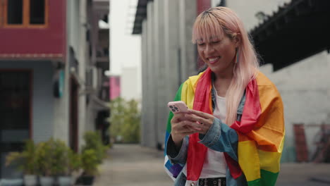 woman using mobile phone, draped in pride flag, in urban setting