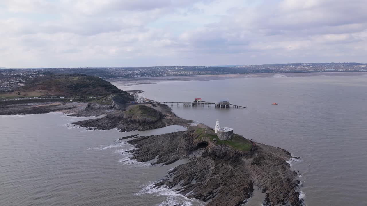 Aerial flyover above lighthouse to the Ferris wheel at Mumbles Pier during sunset, casting long shadows over the coast