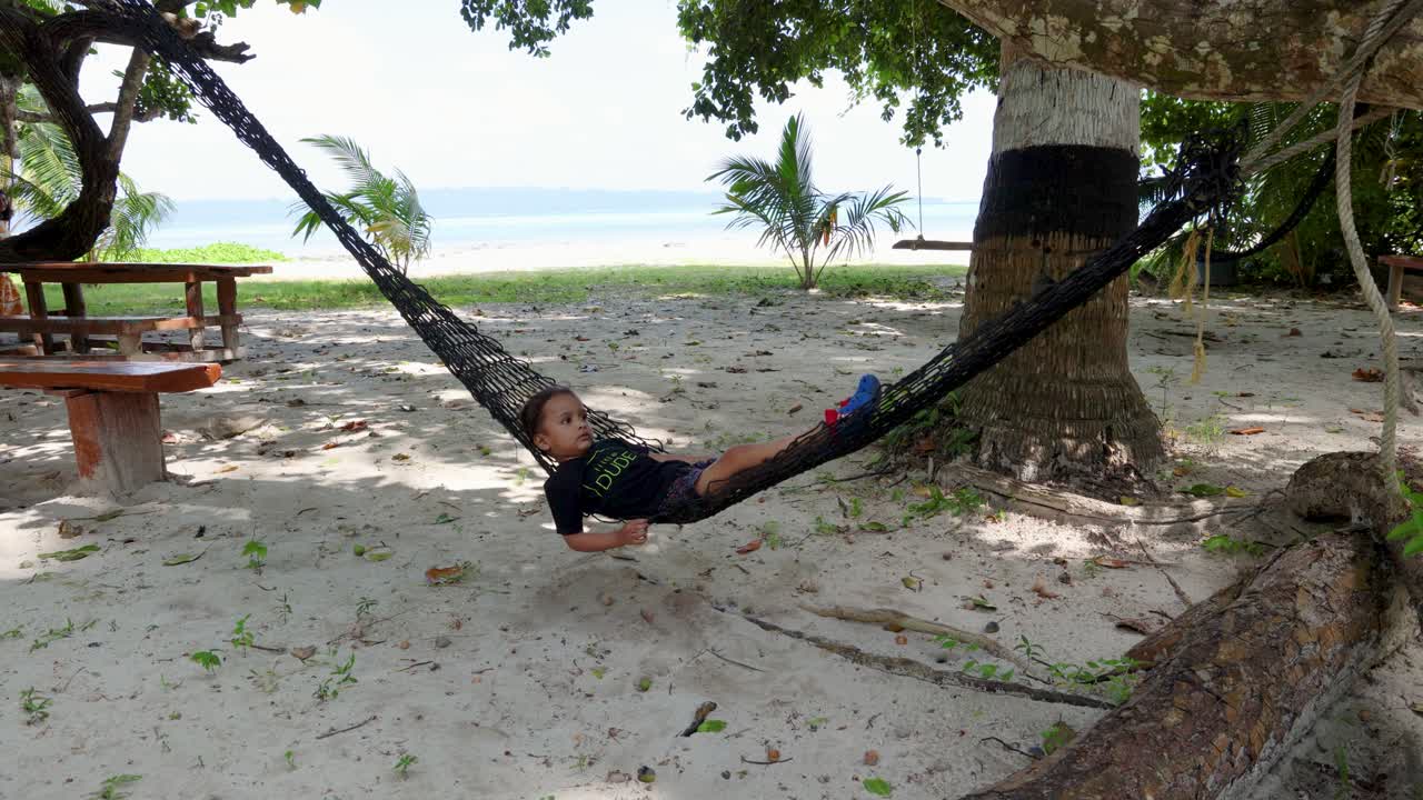 Bambino che si rilassa su un'amaca sotto palme tropicali in spiaggia