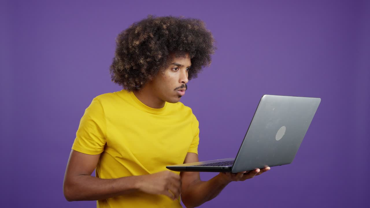 Mann mit lockigem Haar reagiert überrascht und schockiert, während er einen Laptop benutzt