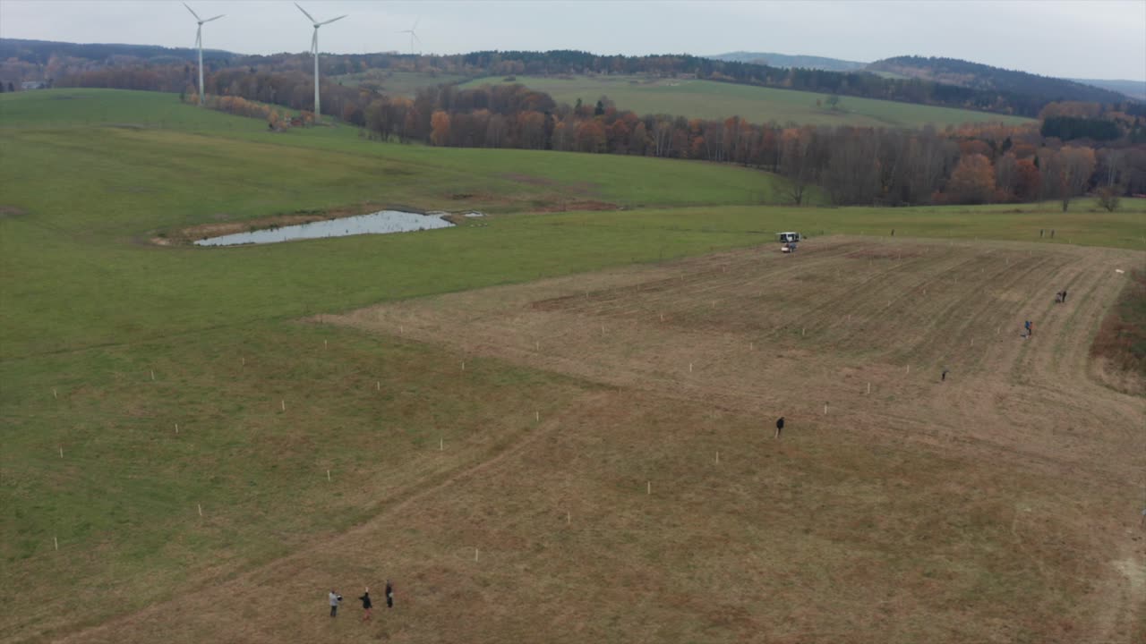 люди сажают новые деревья с ветряными электростанциями на заднем плане