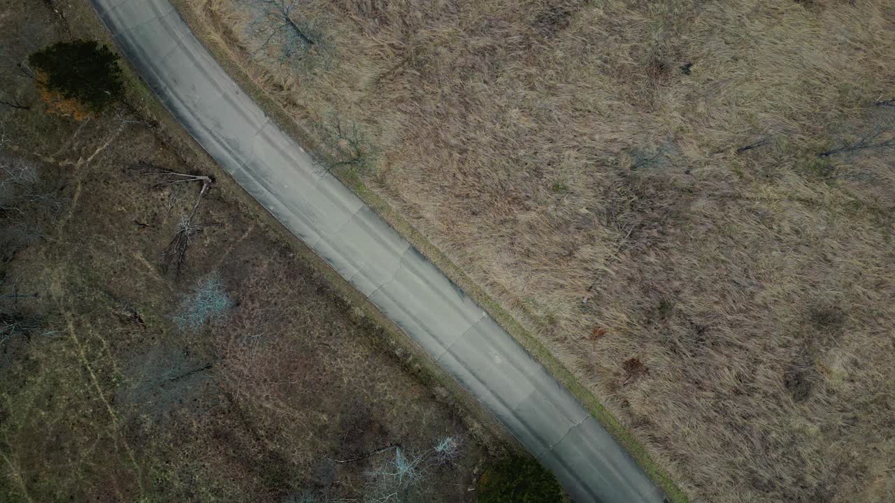 Aerial footage showcasing a winding road through St Francois State Park capturing natural landscape and serene atmosphere. A silver sedan drives by along the grassland