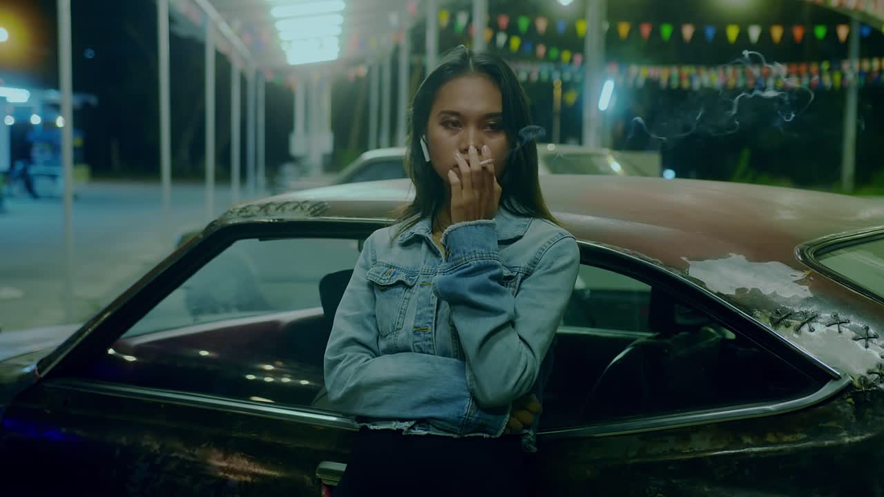 Woman smoking near a vintage car at night