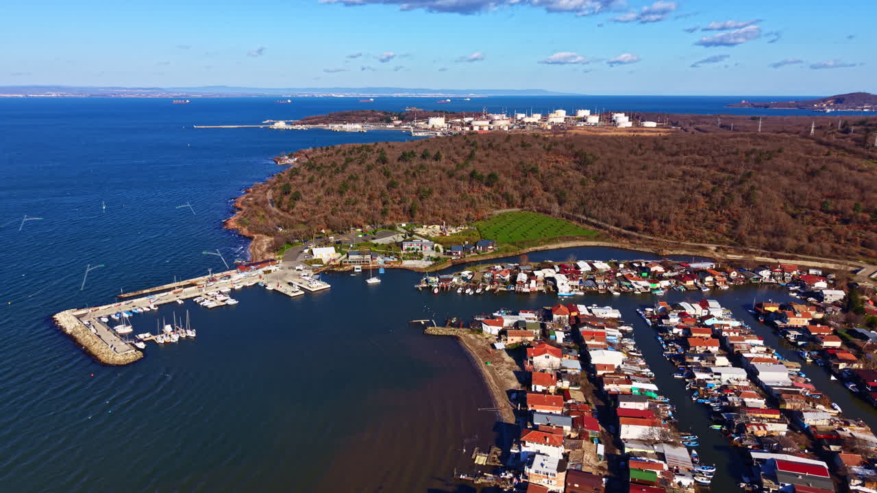 Vista costiera di un piccolo villaggio di pescatori vicino a un porto, circondato da colline e dal mare, con barche ed edifici visibili con tempo sereno.