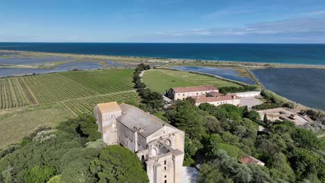 Maguelone-cathedral-near-Mediterranean-coast-of-France-with-lagoon-and-sea-nearby,-Aerial-lowering-orbit-shot