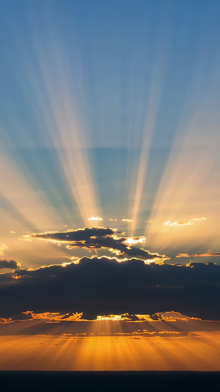 Vertical video: Peeking sun sliding behind cloud bank, casting crepuscular beams over ocean horizon