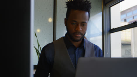 Vista-Frontal-De-Un-Joven-Hombre-De-Negocios-Negro-Trabajando-En-Una-Computadora-Portátil-En-El-Escritorio-De-Una-Oficina-Moderna-4k