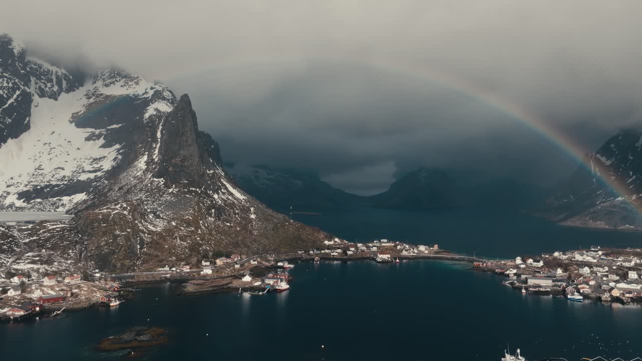 Rainbow Behind Lofoten Peaks In Reine Village, Moskenes Municipality In Nordland County, Norway. Aerial Shot